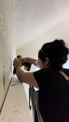 a woman is using a drill to paint the wall