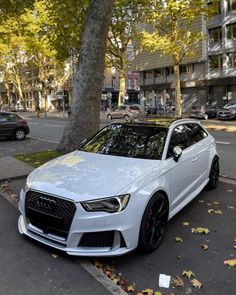 the white car is parked on the side of the street next to some trees and leaves