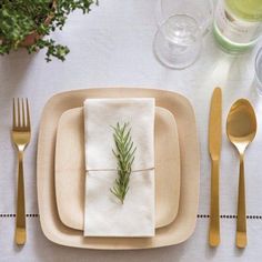 a place setting with silverware, napkins and green sprig on it