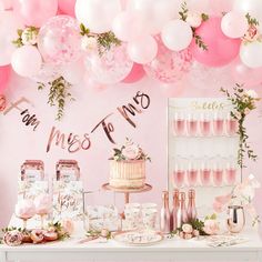 a table topped with lots of pink and white balloons next to a wall covered in flowers