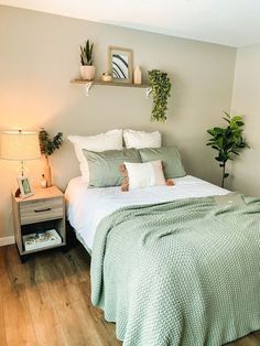 a bed sitting in a bedroom next to a nightstand with two plants on top of it