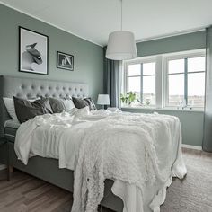 a bedroom with green walls, white bedding and gray curtains on the windowsill