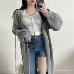 a woman taking a selfie while wearing ripped jeans and a cardigan sweater, holding a camera