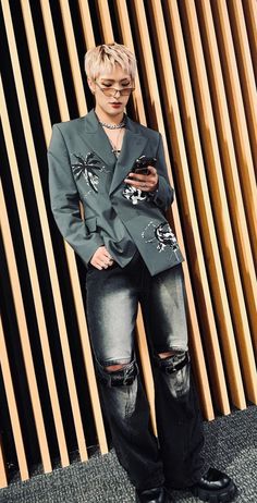 a person standing in front of a wooden wall wearing ripped jeans and a blazer