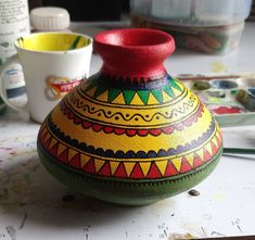 a colorful painted vase sitting on top of a table next to paintbrushes and paints