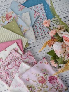 many different types of fabric are laid out on a table with flowers in the background