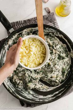 a hand dipping cheese into a bowl of spinach and artichoke sauce in a skillet