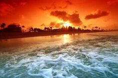 the sun is setting over the ocean with waves crashing in front of it and an orange sky