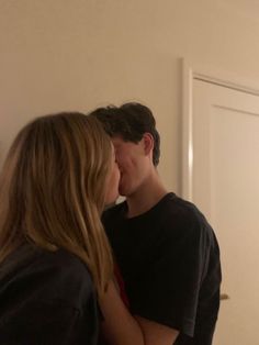 a young man and woman kissing in front of a white door while standing next to each other