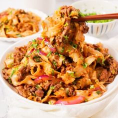 a white bowl filled with noodles and meat on top of a table next to chopsticks