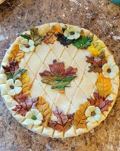 a cake decorated with leaves and flowers on top of a granite countertop in the shape of a pie