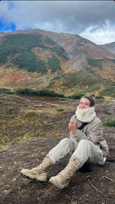 a woman is sitting on the ground with her feet crossed and wearing winter clothing, she is smiling at the camera