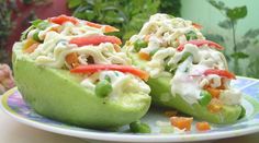 two stuffed avocados are sitting on a plate with vegetables in the center and dressing