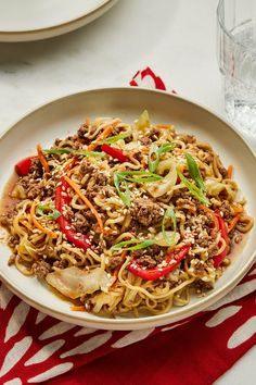 a white plate filled with noodles and meat on top of a red and white table cloth