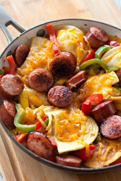 a skillet filled with sausage, peppers and cheese on top of a wooden cutting board