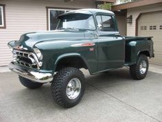 an old green truck parked in front of a house