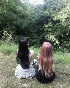 two women sitting on the ground in front of some trees and bushes, one with long black hair