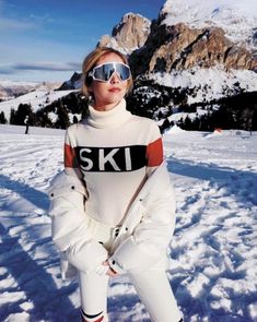 a woman standing in the snow with skis on her feet and goggles on