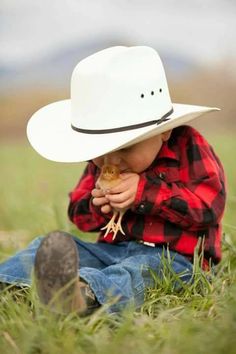 a small child wearing a cowboy hat sitting in the grass