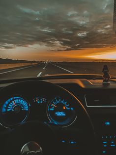 the dashboard of a car driving down an empty highway at sunset or dawn with clouds in the distance