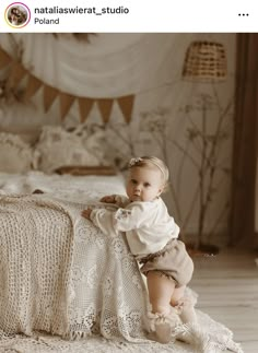 a baby sitting on top of a bed next to a blanket