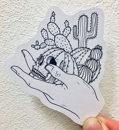 a hand holding up a sticker with a cactus and skull in the center on it