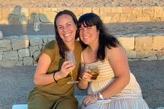 two women sitting next to each other on a bench with wine glasses in their hands