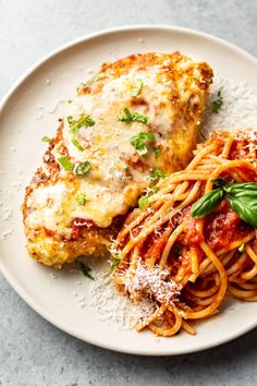 two pieces of chicken parmesan and pasta on a white plate with basil garnish