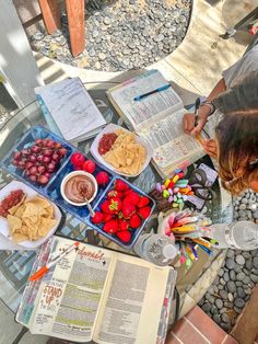 a table topped with lots of food next to an open book on top of a glass table