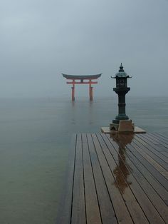 two statues in the water near each other on a wooden pier with foggy skies