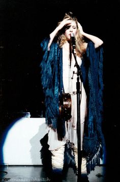 a woman standing in front of a microphone and holding her hands to her head while singing