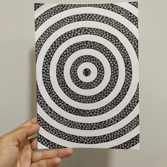 a hand holding up a piece of paper with an image of a spiral design on it