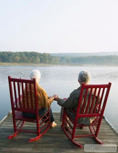 two elderly people sitting on rocking chairs looking out at the water from a dock in black and white