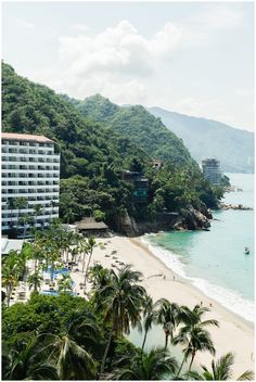 the beach is lined with palm trees and buildings on both sides, along with mountains in the background