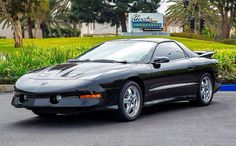 a black sports car is parked in front of a sign and some bushes on the side of the road