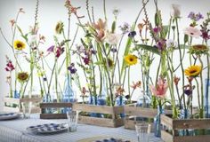 an arrangement of flowers in vases on a table with blue plates and glasses next to each other