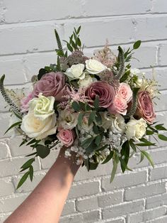 a person holding a bouquet of flowers against a brick wall with white and pink colors