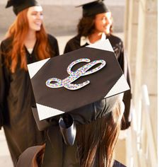 two women in graduation caps and gowns are standing near one another with scissors on their cap