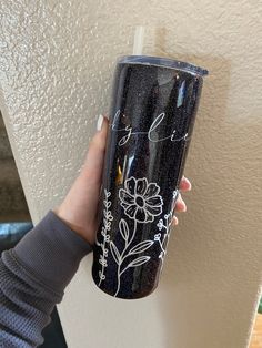 a hand holding a black tumbler with white flowers on it