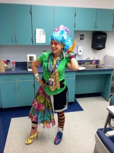 a woman with blue hair in a green shirt and colorful wig standing in a kitchen