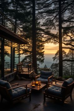 two chairs and a table on a deck near some trees at sunset with the sun setting in the distance