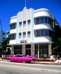 a pink car parked in front of a tall building on the side of the road