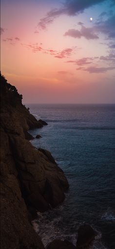 the sun is setting over the ocean and rocks