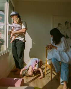 a man standing next to a woman holding a baby in front of a window with other people looking out the window