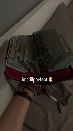 a person holding a red book with stacks of money on top of it in their hand