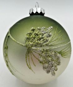 a green ornament with silver glitters on it's side and a white background