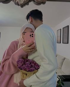 a man and woman taking a selfie with flowers in front of their face while holding a cell phone