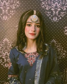 a woman wearing a blue dress and headpiece standing in front of a patterned wall