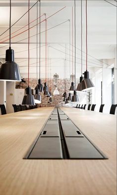 a long table with black chairs and hanging lights