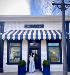 a woman standing in front of a store with blue and white striped awnings